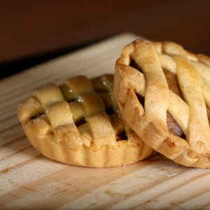 Two delicious homemade mini apple pies with a lattice top on a wooden cutting board, perfect for a sweet treat.